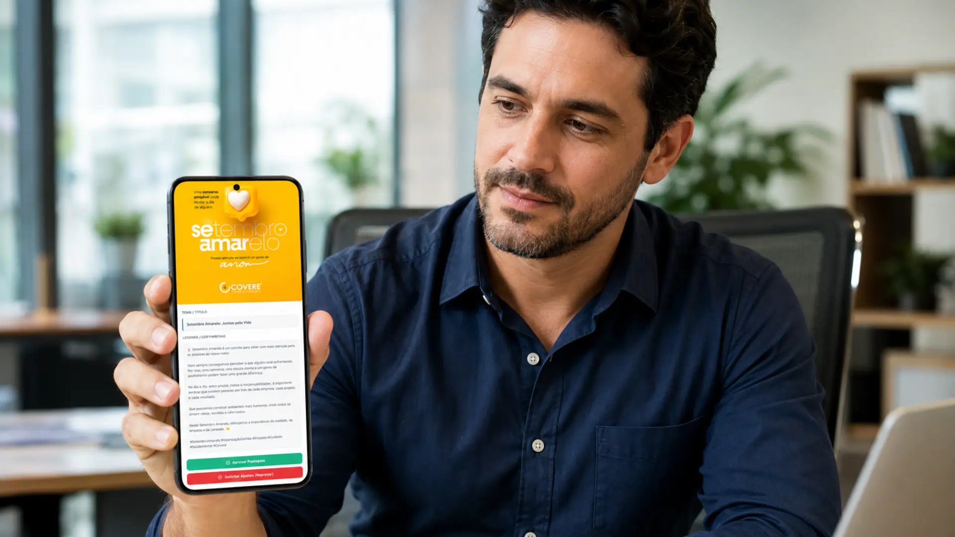 Homem em um escritório analisa pelo celular uma postagem da campanha Setembro Amarelo, com o conteúdo, a legenda e as opções “Aprovar Postagem” e “Solicitar Ajustes” visíveis na tela.